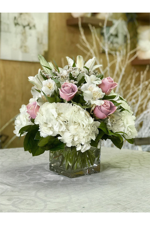 A floral arrangement featuring pink roses and white flowers in a clear vase, with greenery.