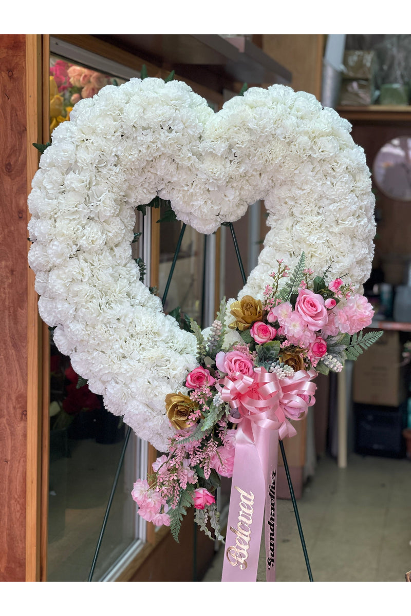 Open heart funeral wreath with white artificial carnations and pink rose accents on a standing easel – Eclore Floral NJ