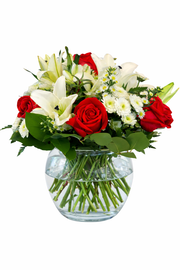 Pink rose and white lily bouquet in clear glass vase with greenery on white background
