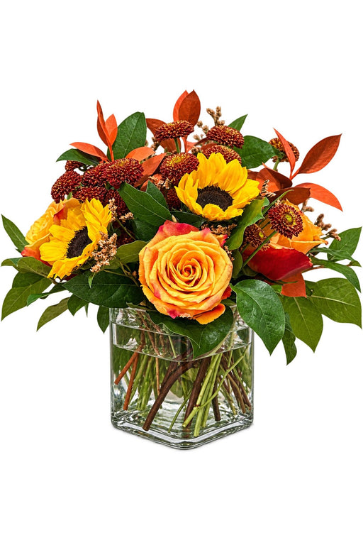 Autumn bouquet with sunflowers, orange roses, chrysanthemums, and seasonal foliage in a clear square vase