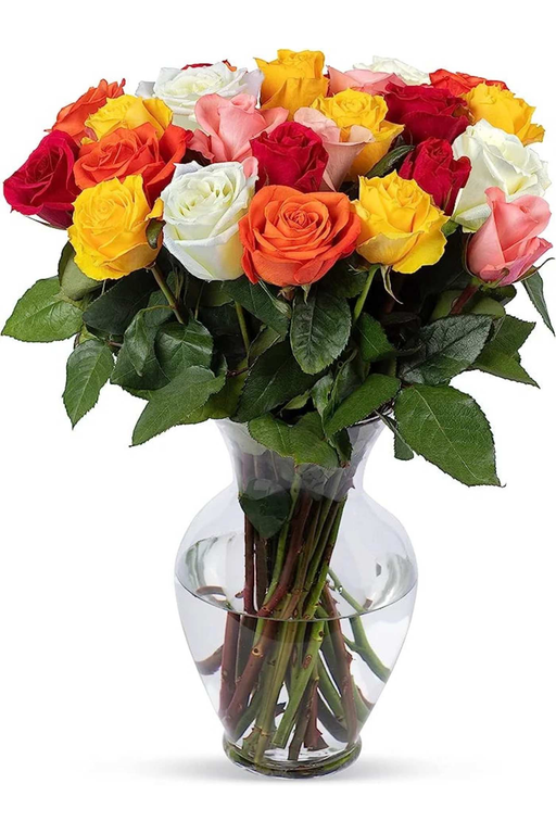 Red, orange, yellow, pink and white roses with green foliage in a clear glass vase