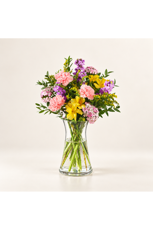 Petal Confetti: pink, yellow and purple flowers with greenery arranged in a clear glass vase against a warm ivory background.