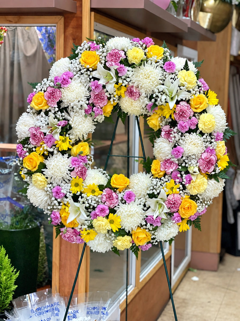Standing funeral wreath of yellow roses, lavender carnations, white chrysanthemums and lilies on an easel
