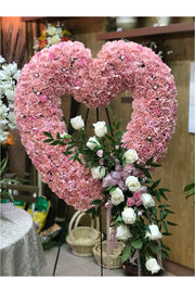 Pink open-heart standing funeral spray made of pink carnations, white roses, and greenery with cascading floral accents.