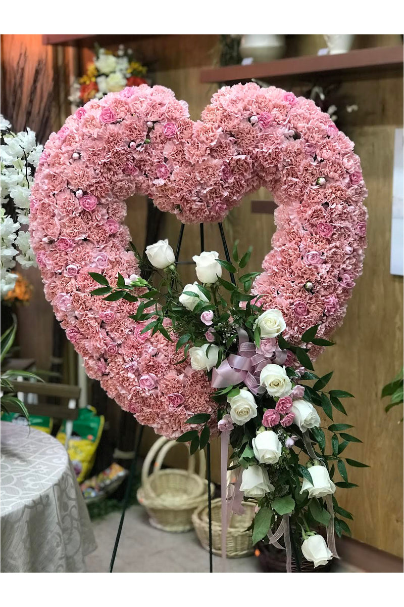 Pink open-heart standing funeral spray made of pink carnations, white roses, and greenery with cascading floral accents.