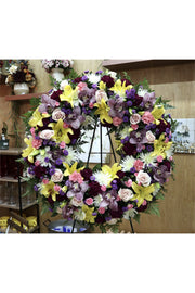Purple and yellow funeral wreath with lilies, roses, orchids, and mixed blooms on a standing easel