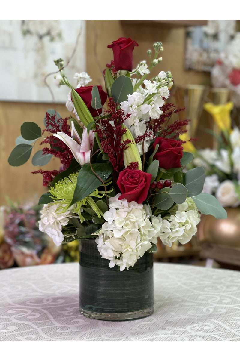 Crystal Rose arrangement with red roses, white hydrangeas, lilies, green mums, and eucalyptus in a modern vase