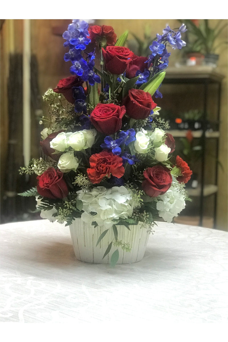 Red, white, and blue patriotic flower arrangement with roses, hydrangeas, and delphinium in a white vase – New Jersey florist.