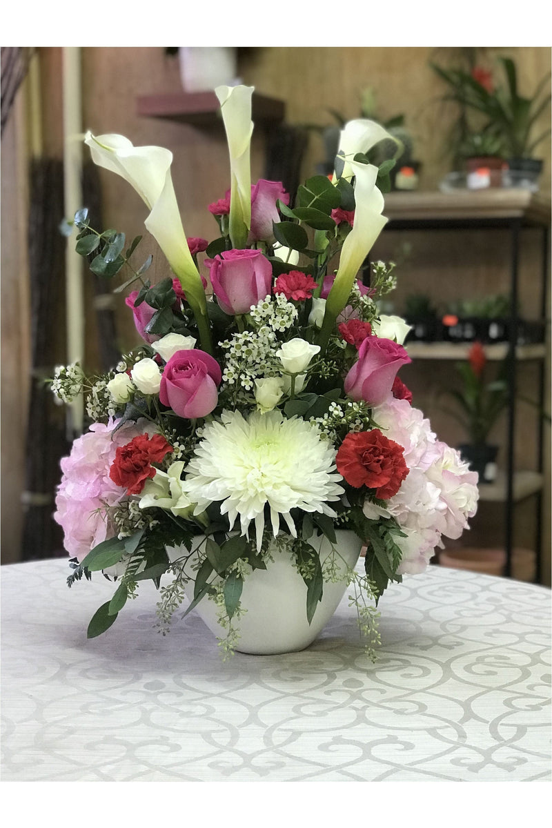 Lilly Shake arrangement with calla lilies, pink roses, carnations, hydrangea, and a dahlia in a white vase.