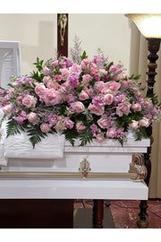 Heavenly Pink Rose Tribute Casket Spray featuring pink roses, lavender blooms, and lush greenery arranged beautifully on a white casket.