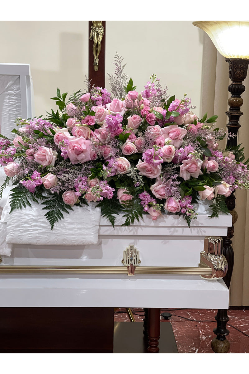 Heavenly Pink Rose Tribute Casket Spray featuring pink roses, lavender blooms, and lush greenery arranged beautifully on a white casket.