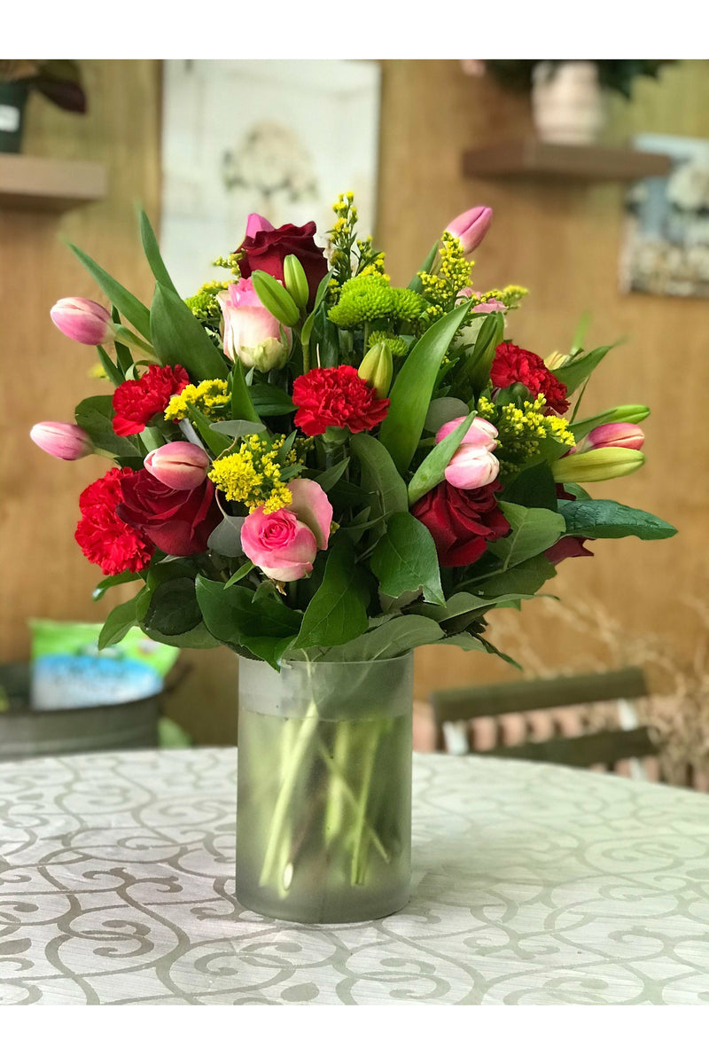 May Flowers arrangement featuring pink tulips, roses, red carnations, and bright green accents in a frosted vase. Handcrafted by Eclore Floral with delivery in Hackensack NJ.