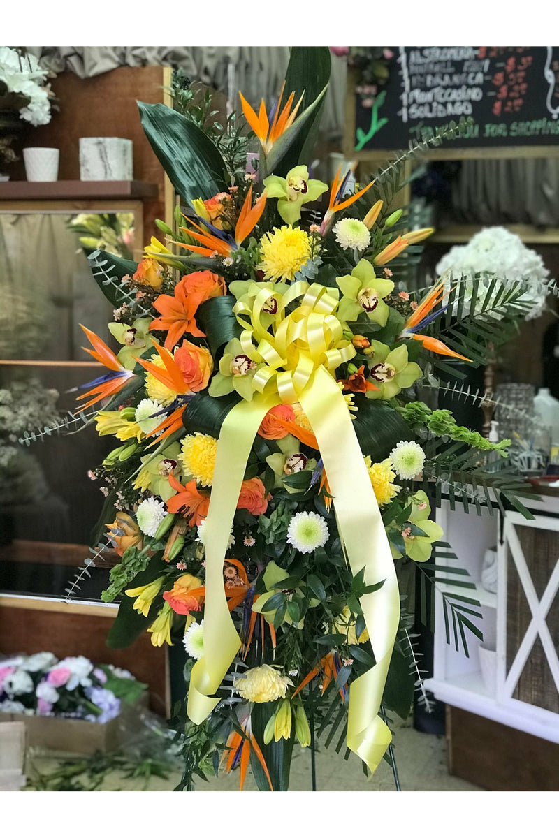 Tropical Bird of Paradise funeral standing spray with orange roses, orchids, yellow mums, and yellow ribbon