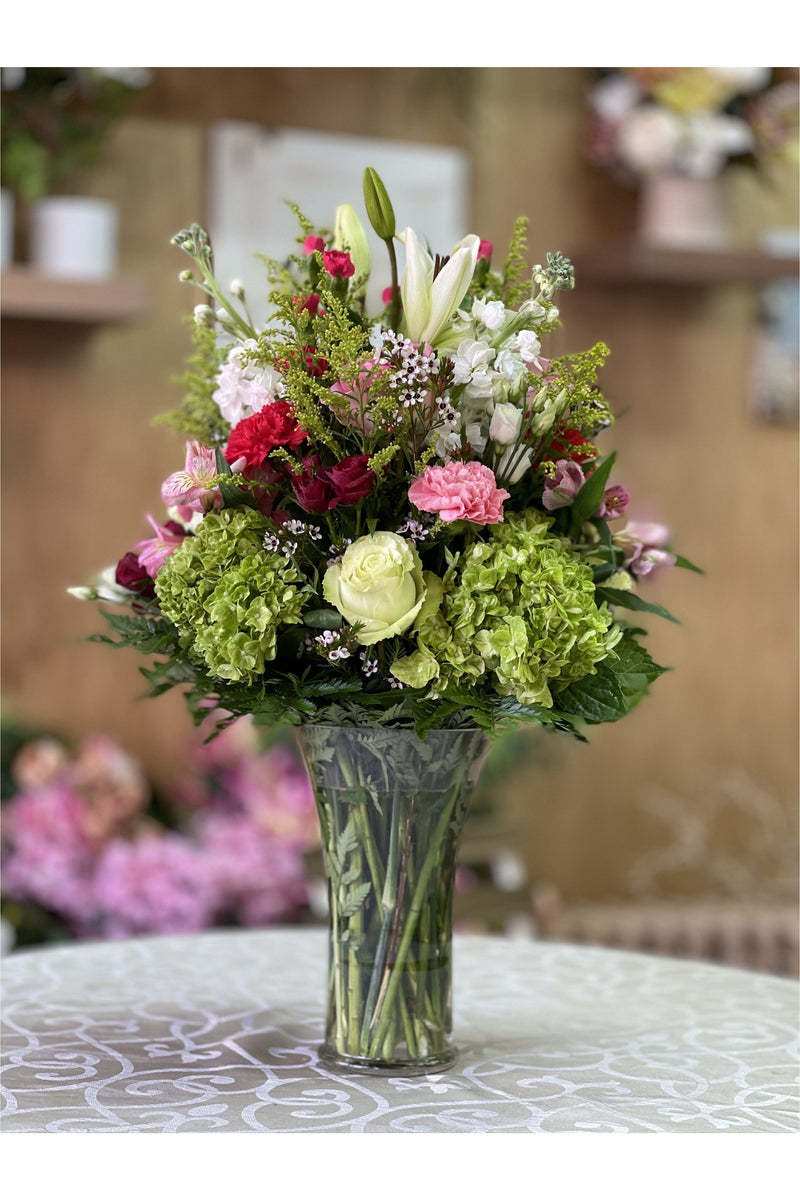 Green hydrangea and berry-accented flower arrangement with roses, lilies, and carnations in a tall vase – New Jersey florist.