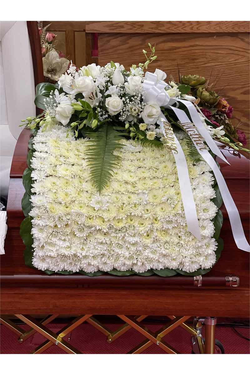 White funeral blanket casket spray made of fresh chrysanthemums, roses, lilies, and baby’s breath.