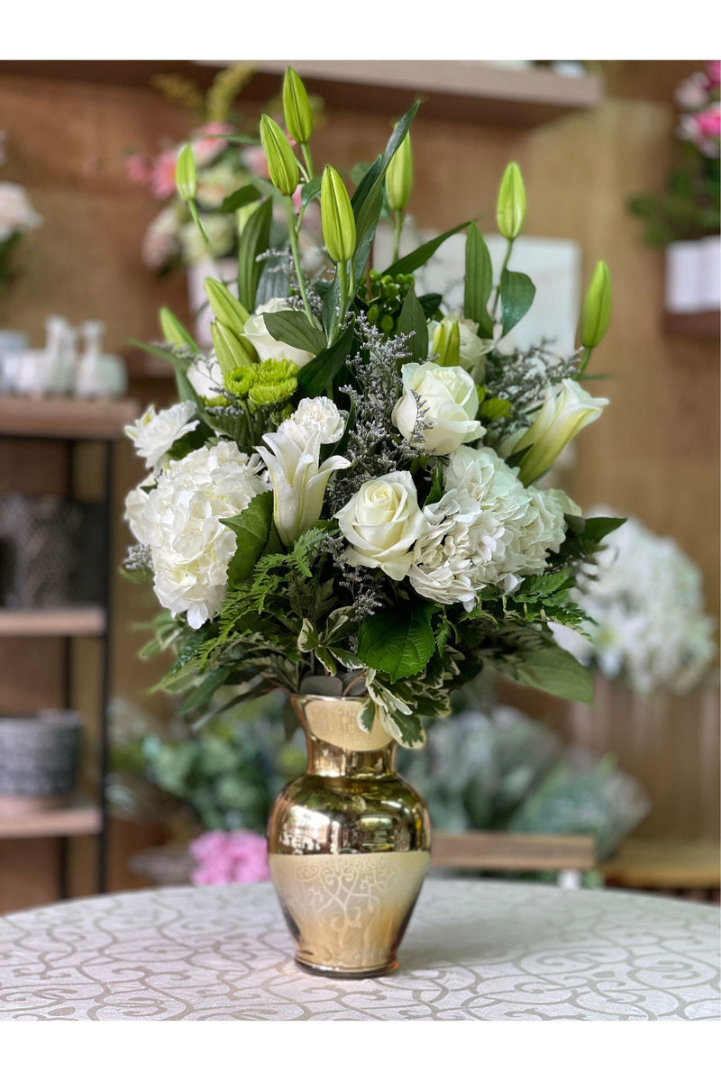 White Chocolate arrangement with white lilies, roses, hydrangeas, and greenery in a gold vase, handcrafted by Eclore Floral.