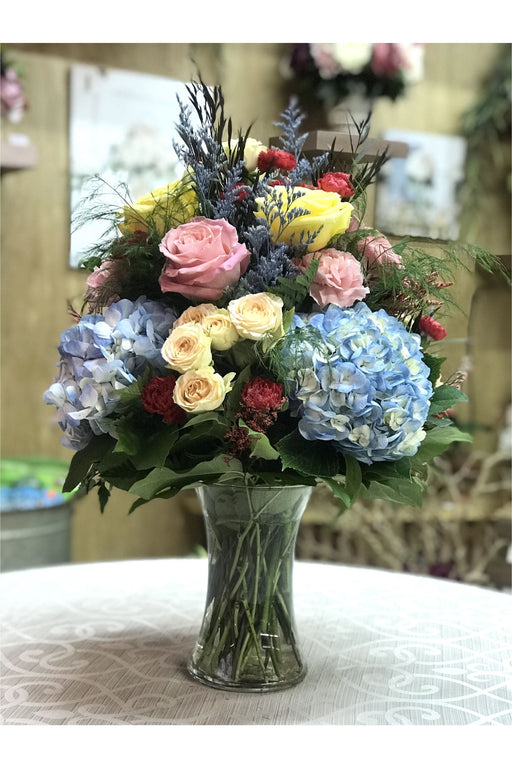 Iris Spring flower arrangement with pastel roses, blue hydrangeas, and mixed seasonal blooms in a clear vase, handcrafted by Eclore Floral New Jersey.
