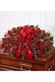 Red rose funeral casket spray with lush greenery and red satin bow
