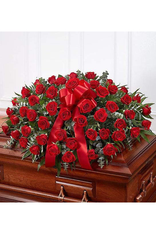 Red rose funeral casket spray with lush greenery and red satin bow