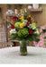 Tropical mixed flower arrangement in a glass vase featuring roses, green hydrangea, Birds of Paradise, lilies, and carnations.