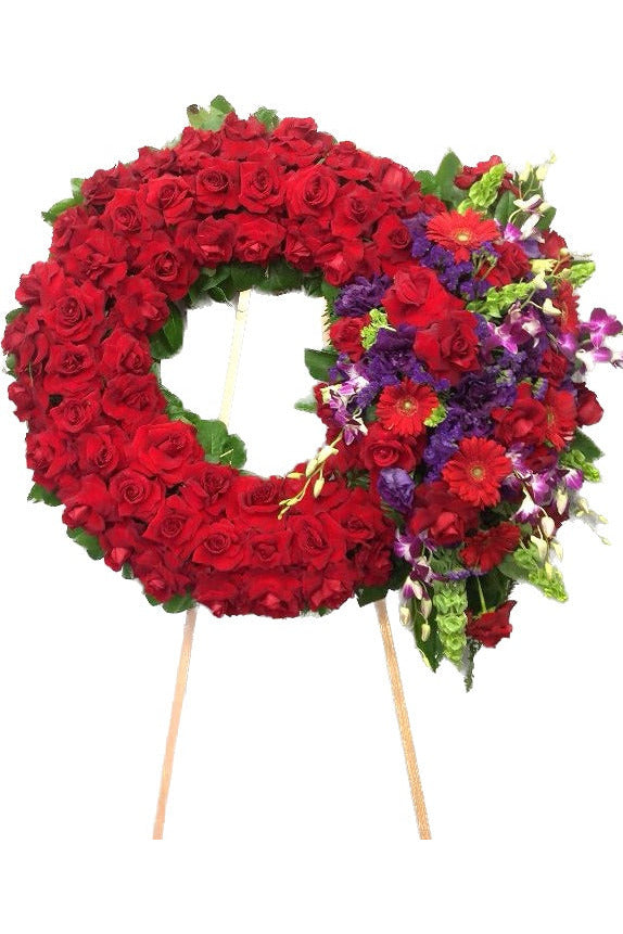 Red rose funeral wreath with natural purple floral accents on standing easel