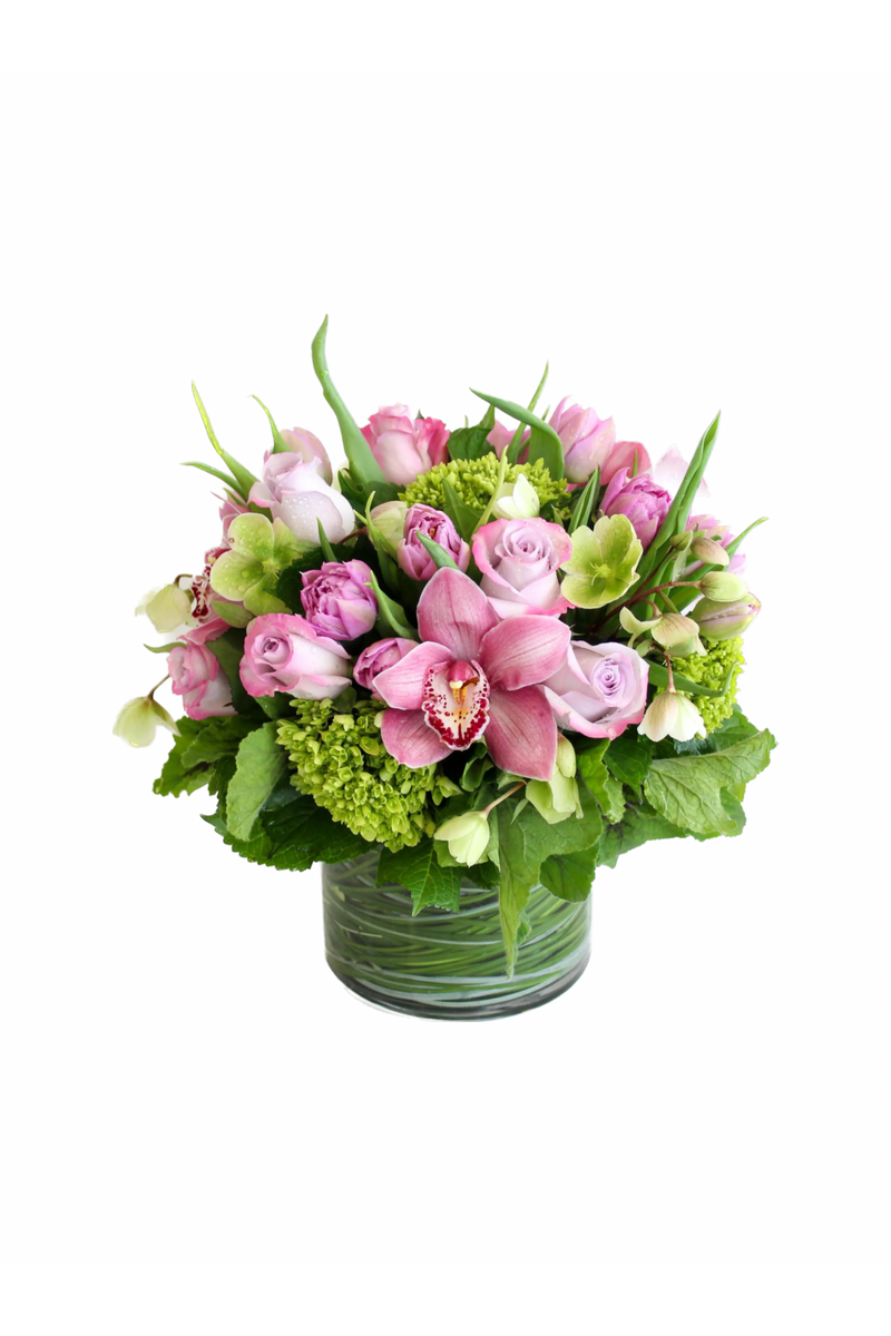 Pink and green luxury flower arrangement with orchids, roses, tulips, and hydrangea in a clear glass vase.